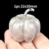 A smooth, light gray natural stone pumpkin figurine with a stem is held in a hand.