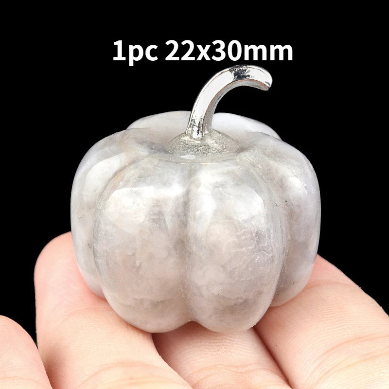 A smooth, light gray natural stone pumpkin figurine with a stem is held in a hand.
