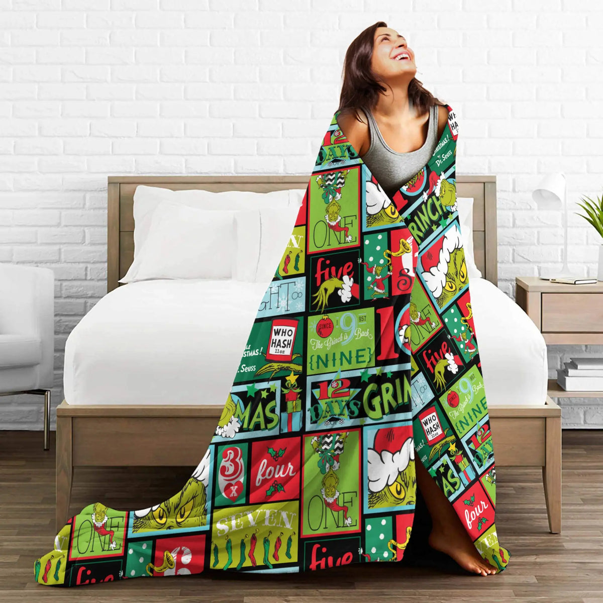 A woman is smiling while lying on a bed with a colorful patterned coral fleece throw blanket draped over her.