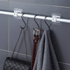 Silver curtain rod hooks mounted on a gray tile wall, with a black chain and a dark leather strap hanging from them.