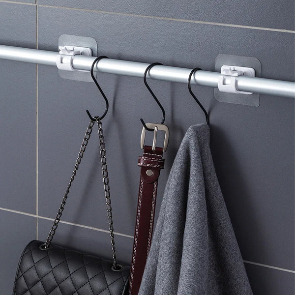 Silver curtain rod hooks mounted on a gray tile wall, with a black chain and a dark leather strap hanging from them.