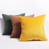 Three velvet throw pillows in shades of olive green, rust brown, and mustard yellow.