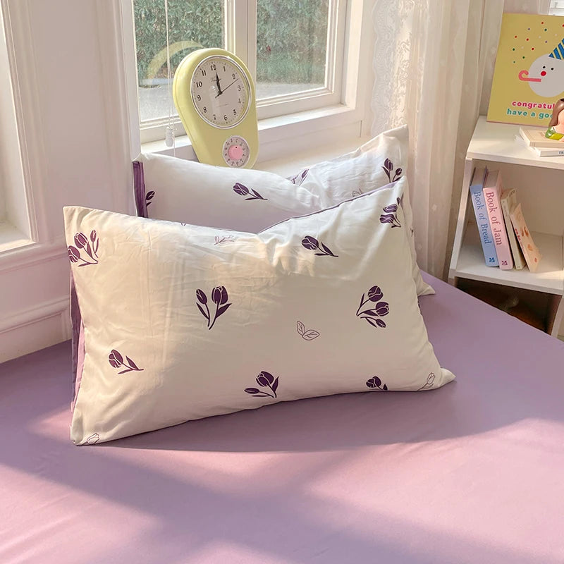 A light purple duvet cover set with white pillowcases and a yellow alarm clock on a bed.