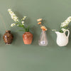 Three small ceramic vases holding white flowers displayed against a muted green background.