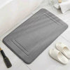 A gray ultra soft memory foam bathroom mat is shown next to a pair of white slip-on shoes.