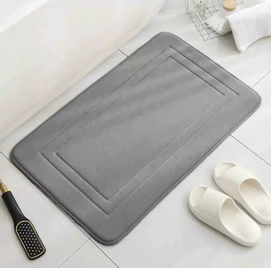 A gray ultra soft memory foam bathroom mat is shown next to a pair of white slip-on shoes.
