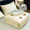 A cream-colored embroidered cooling summer quilt folded neatly on a table next to a lamp.