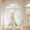White sheer floral lace curtain hanging over a window in a bright room.