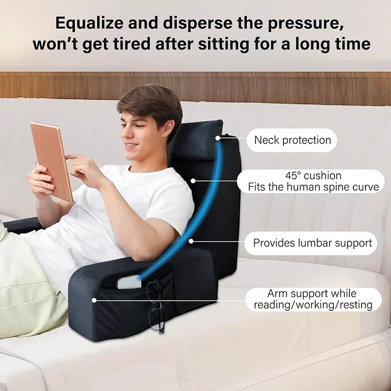 A young man is using an ergonomic back support pillow with armrests while reading on a tablet on a sofa.