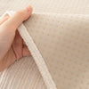 A hand is holding a beige geometric chenille sofa cushion cover, showing the textured fabric and stitching.