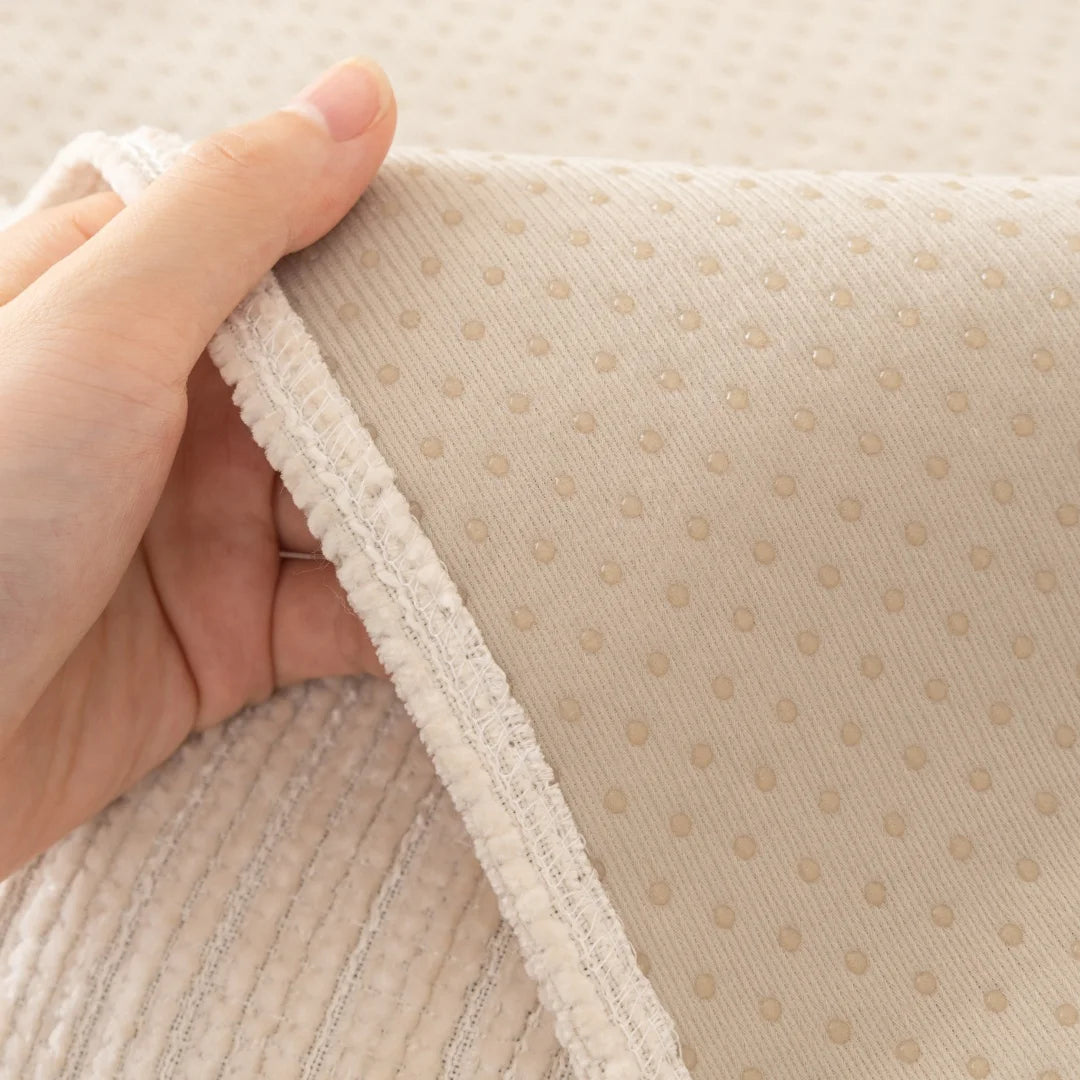 A hand is holding a beige geometric chenille sofa cushion cover, showing the textured fabric and stitching.