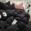 A black duvet cover set with a pink pillow and a black stuffed animal resting on a bed.
