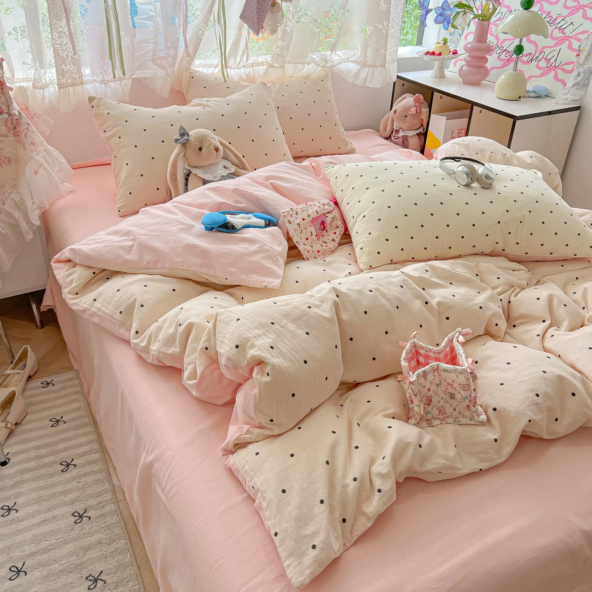 A pink polka dot duvet cover set with matching pillowcases and stuffed animal toys on a bed.