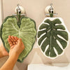 A hand towel with an embroidered leaf design hanging on a rack.