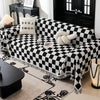 A black and white checkerboard sofa slipcover draped over a sofa, with a patterned rug and a dark table nearby.