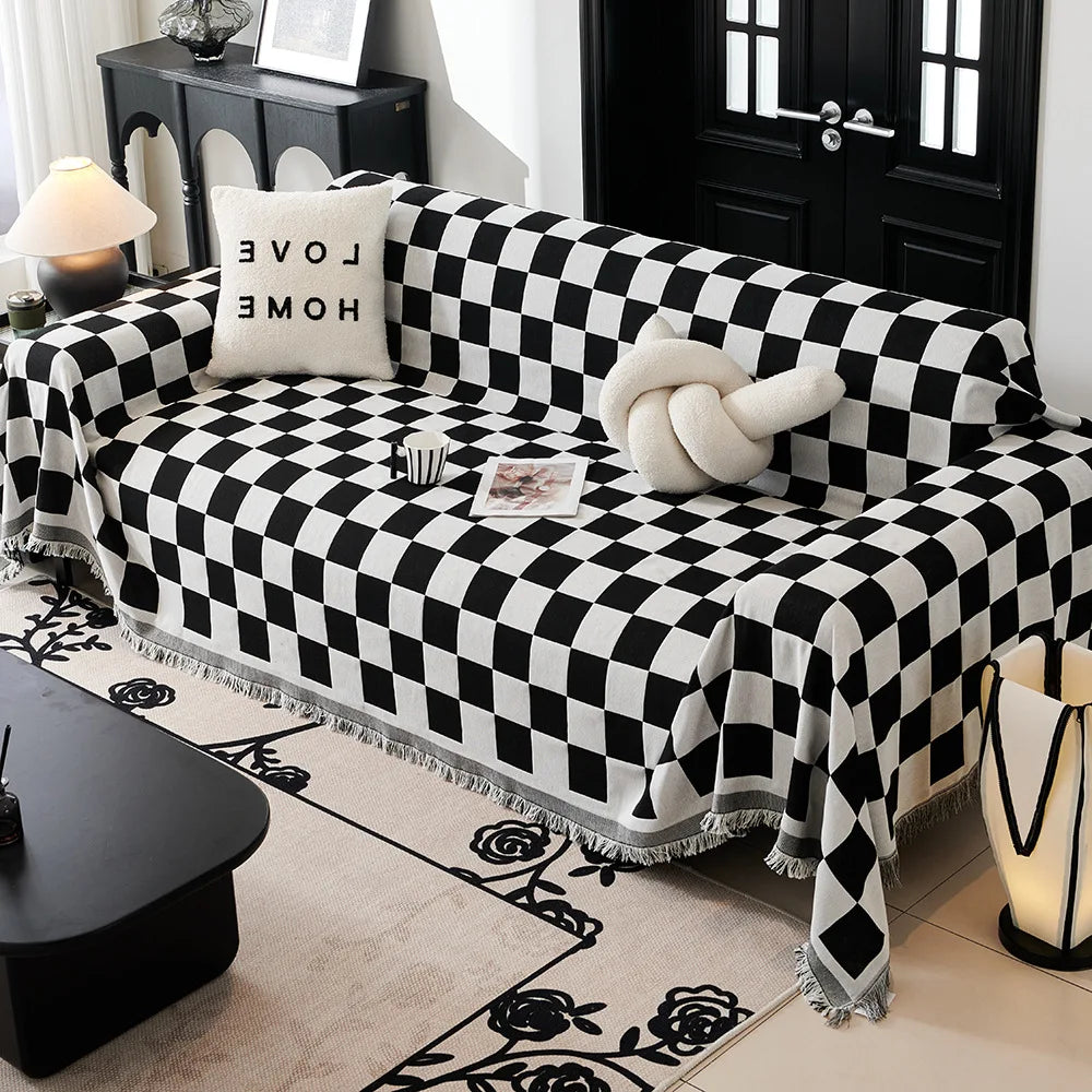 A black and white checkerboard sofa slipcover draped over a sofa, with a patterned rug and a dark table nearby.