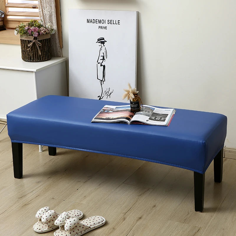 A blue waterproof stretch dining bench cover placed on a wooden bench with magazines and a framed drawing.