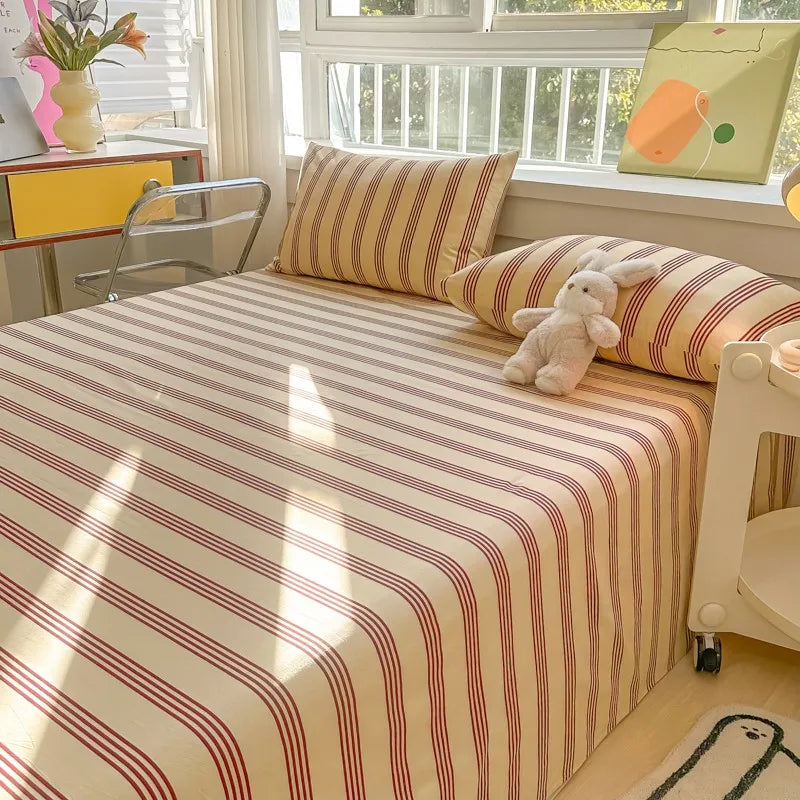 A bed with striped bedding in beige and red, featuring a yellow pillow and a white stuffed rabbit.