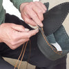 Hands are using a sewing needle to work on dark leather fabric.
