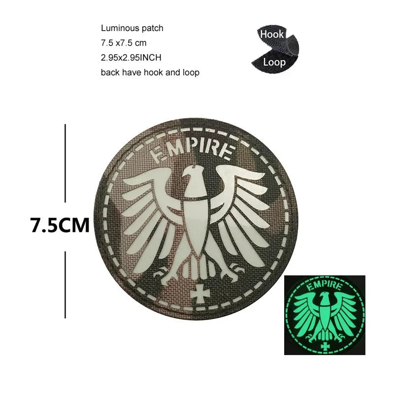 A round, dark embroidered patch featuring a white eagle shield design with the word EMPIRE and a cross.