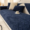 A dark navy blue plush winter sofa cushion cover with light beige accent pillows and a white cup on the fabric.