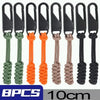 A set of black zipper pulls with green, orange, and beige cord sliders for bags and clothing.