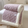 A thick, quilted mauve fleece blanket with white sherpa trim is folded on a white bed.