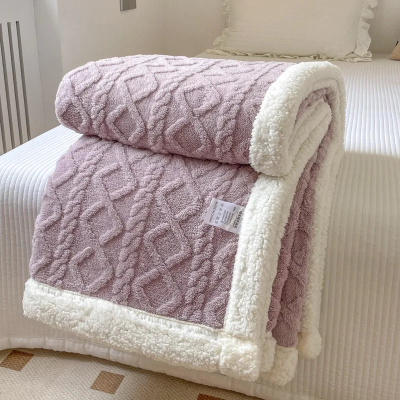 A thick, quilted mauve fleece blanket with white sherpa trim is folded on a white bed.