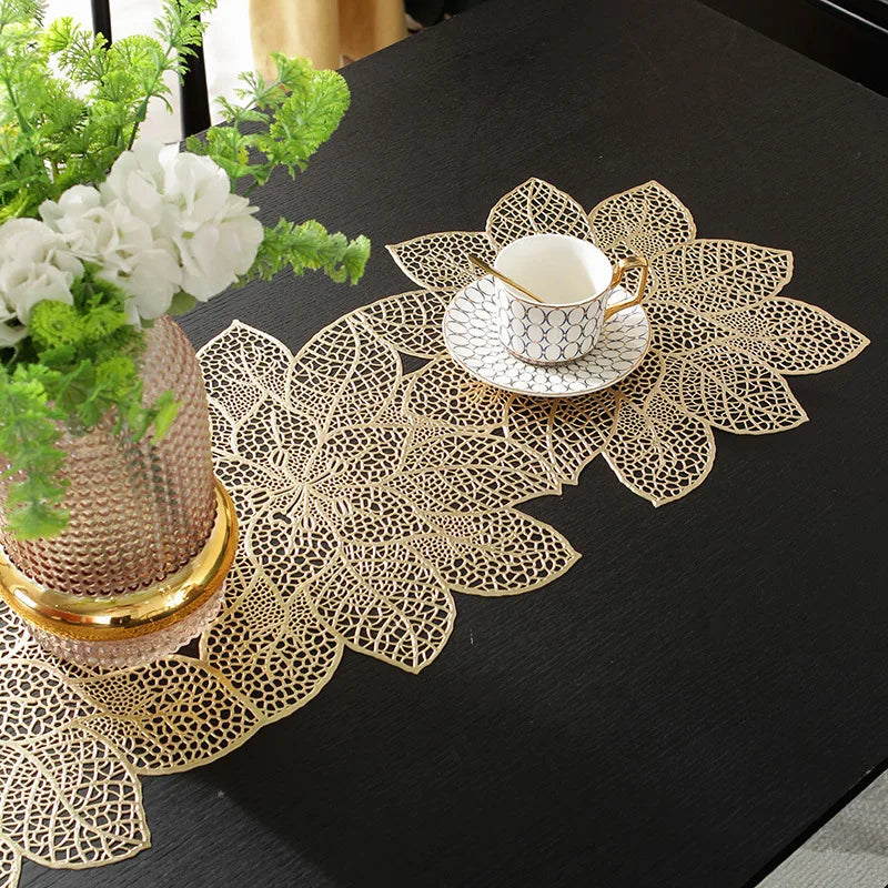 Gold leaf patterned placemat with a white teacup and greenery on a black table.