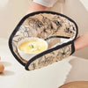 A pair of floral heat-resistant oven mitts is shown being held, featuring a patterned fabric and black trim.