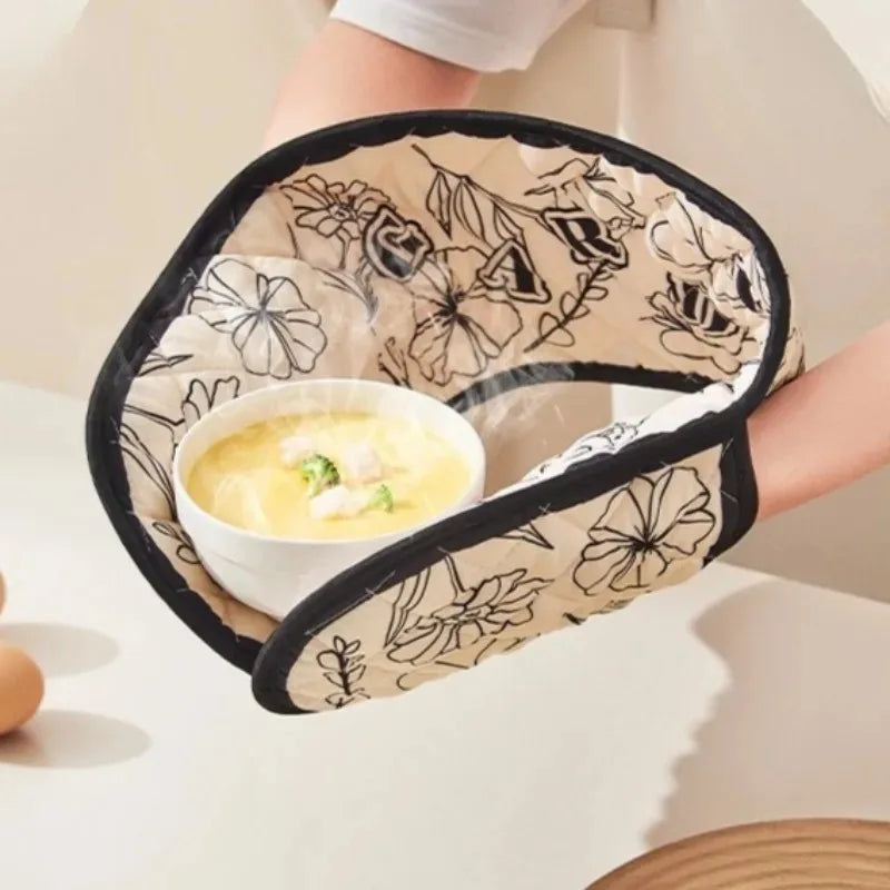 A pair of floral heat-resistant oven mitts is shown being held, featuring a patterned fabric and black trim.
