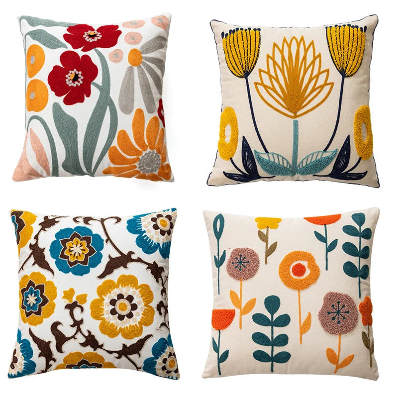 Four throw pillows featuring embroidered floral patterns in orange, red, yellow, and teal on a cream background