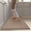 A person wearing light pants is standing on a rectangular beige non-slip faux sisal kitchen rug in a modern kitchen.