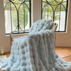 A light blue plush faux fur throw blanket draped over a metal hanger in front of a window.