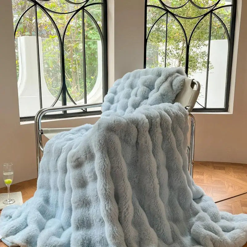 A light blue plush faux fur throw blanket draped over a metal hanger in front of a window.