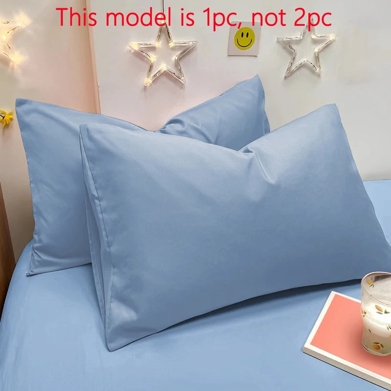A light blue matte solid color pillowcase is displayed on a bed, with decorative star-shaped wall hangings visible.