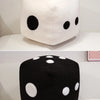 A black dice plush pillow with white dots, displayed on a white surface.