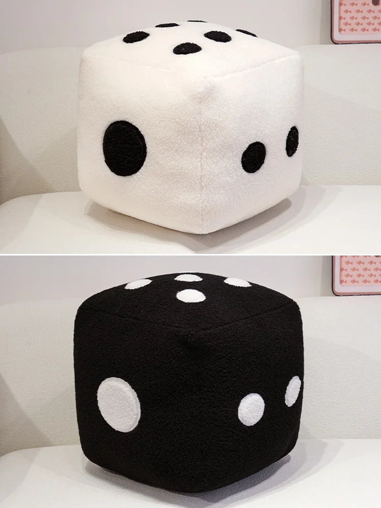 A black dice plush pillow with white dots, displayed on a white surface.