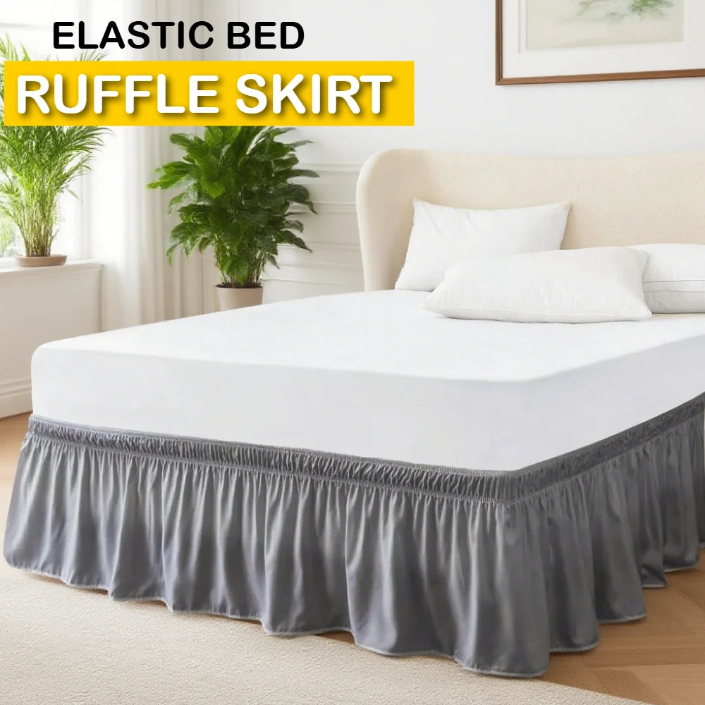 A white bed with a ruffled gray elastic skirt and white pillows on a light wood floor.