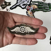 A hand holds several embroidered patches, including an army insignia and a winged emblem.