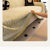A close-up of an elegant beige jacquard sofa cover blanket with green fringe and a black butterfly accent.