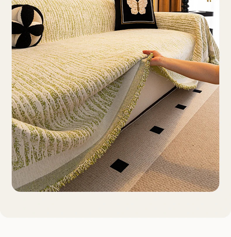 A close-up of an elegant beige jacquard sofa cover blanket with green fringe and a black butterfly accent.