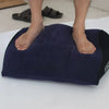 A dark blue inflatable body support pillow is placed on a white surface with bare feet visible.
