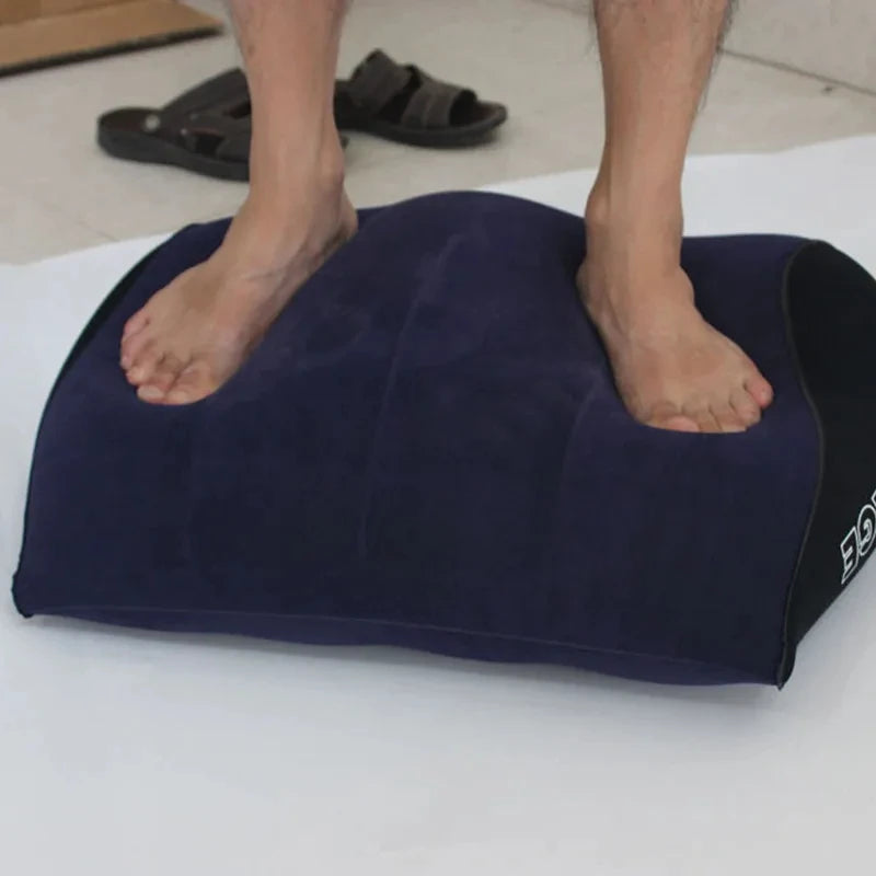 A dark blue inflatable body support pillow is placed on a white surface with bare feet visible.