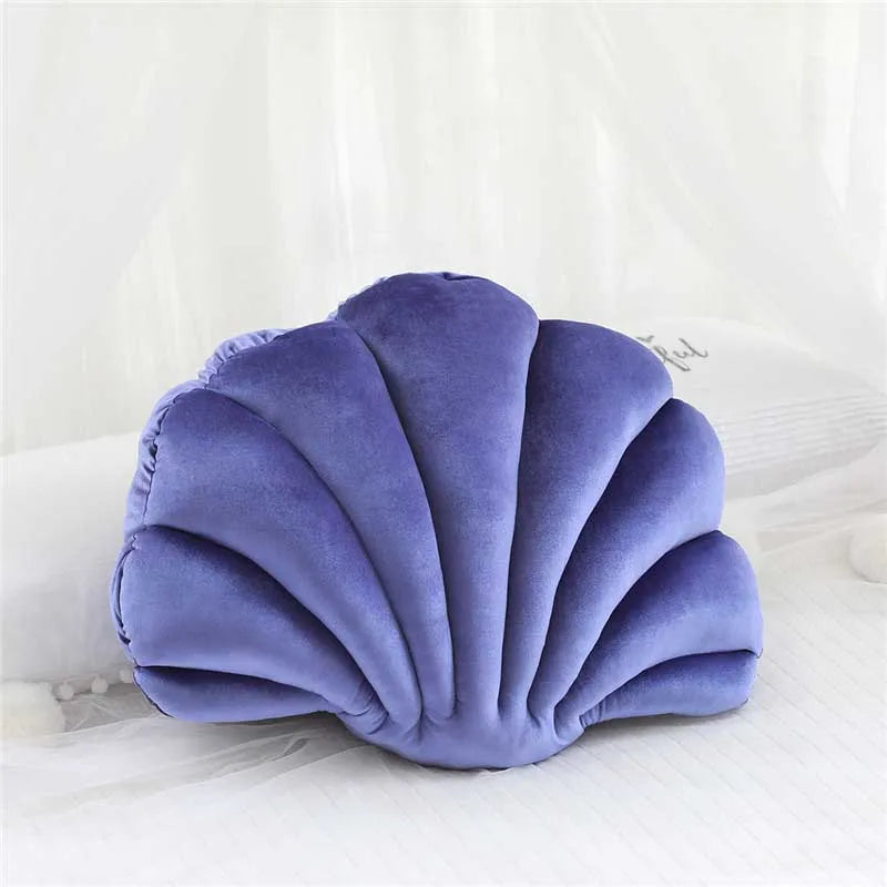A purple velvet stuffed sofa cushion shaped like a decorative seashell resting on white bedding.