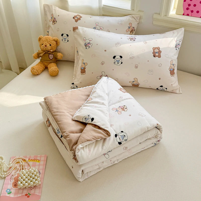 A white quilted blanket with a light pink lining and small animal patterns is displayed on a light surface.