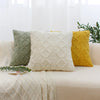A set of three geometric plaid cushion covers in sage green, cream, and mustard yellow displayed on a light-colored sofa.