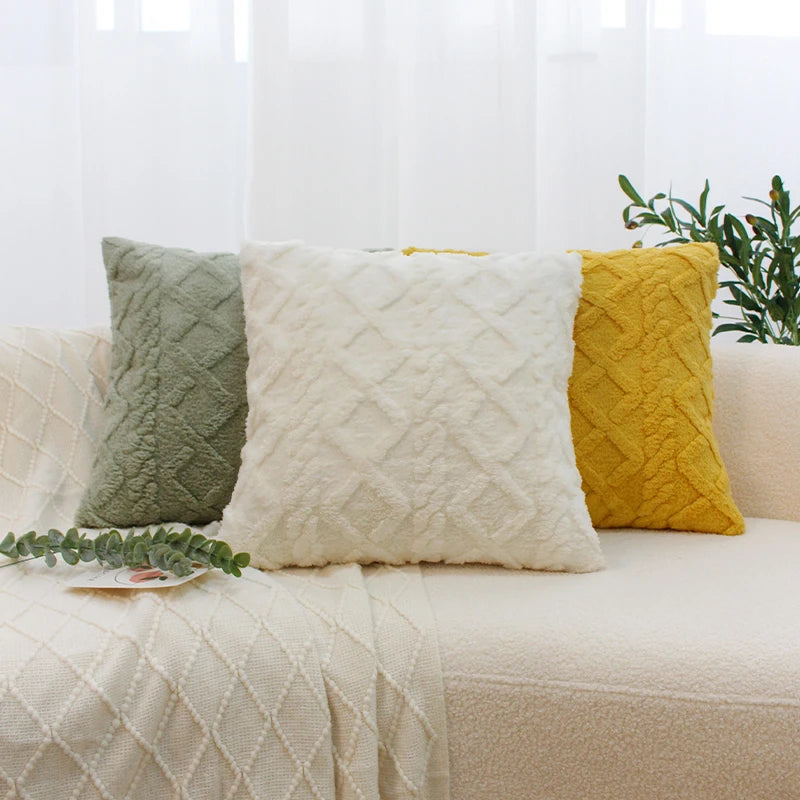 A set of three geometric plaid cushion covers in sage green, cream, and mustard yellow displayed on a light-colored sofa.