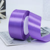 Roll of purple satin craft ribbon shown next to a gray card.