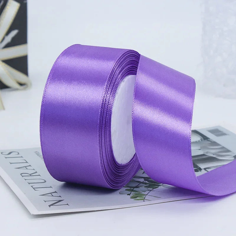 Roll of purple satin craft ribbon shown next to a gray card.